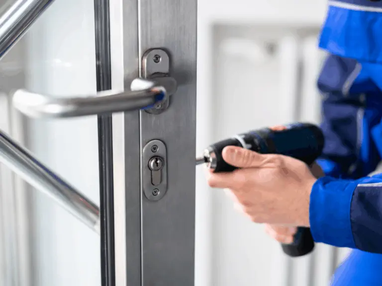Person in blue uniform using a power drill to install or repair a lock on a metal and glass door, ensuring security while replacing locks.