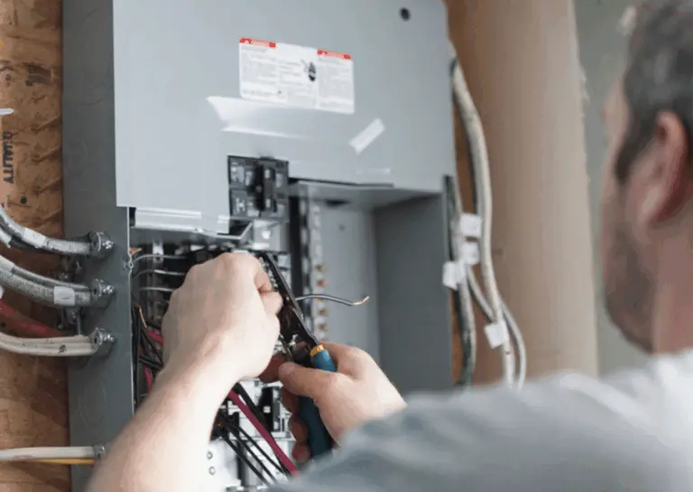 A person uses pliers to work on the wiring inside an open electrical panel, ensuring safe home security for BC homeowners.