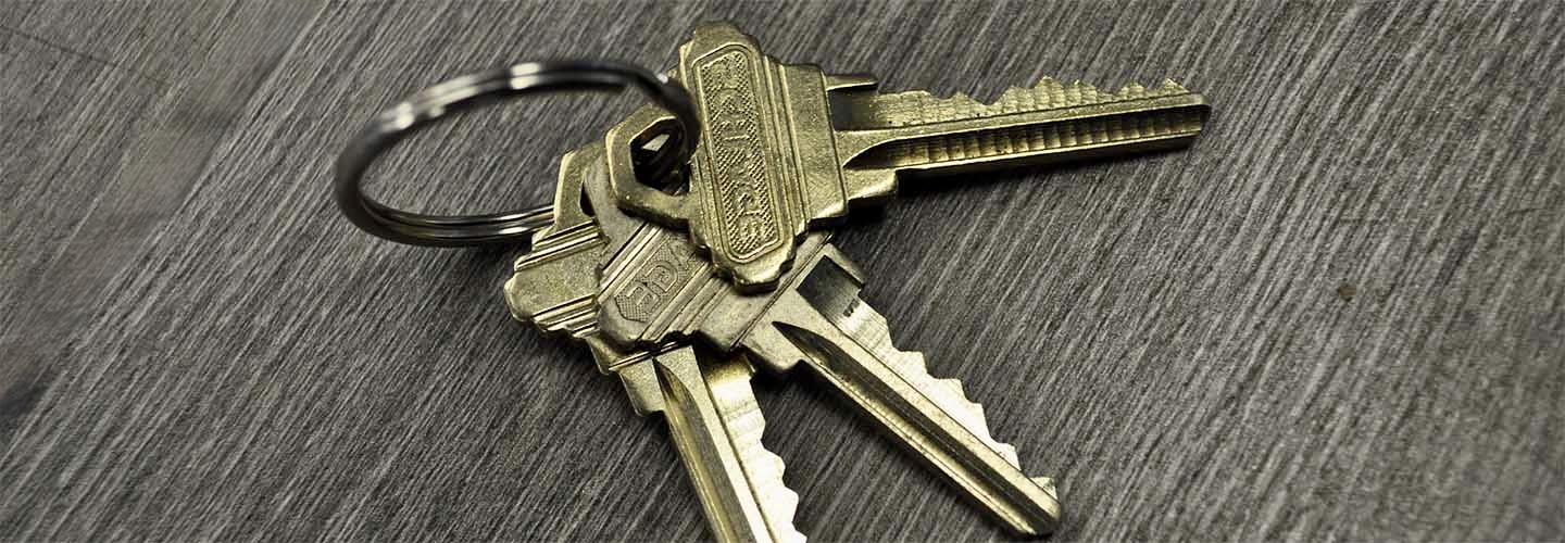 A set of five brass keys on a metal keyring placed on a gray wooden surface.
