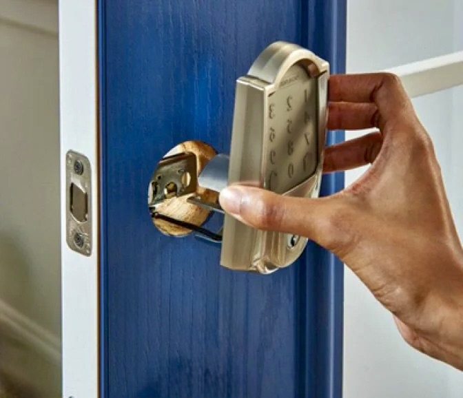 A person installs a keypad smart lock onto the inner side of a blue door.
