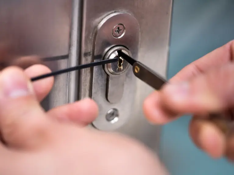 Close-up of hands using lock picking tools to manipulate the lock mechanism in a metal door, showcasing the skill and precision of a professional locksmith Vancouver.