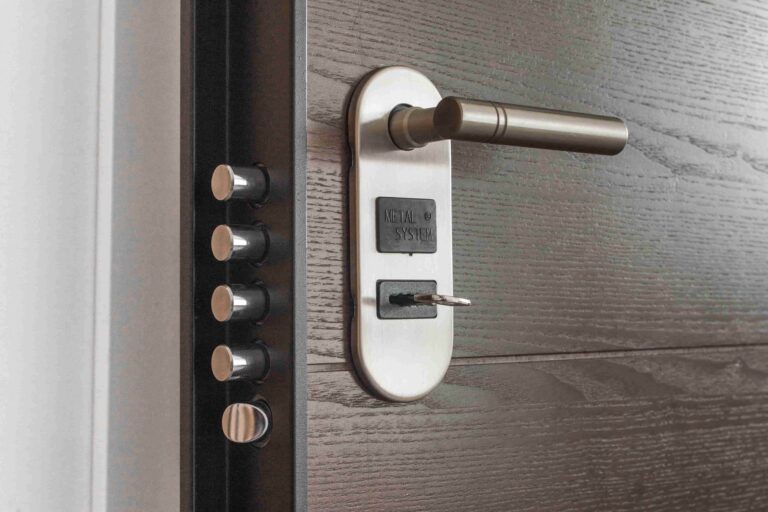 A close-up of a metal door lock system with four cylindrical deadbolts extended and a key inserted into the lock on a dark wooden door, showcasing the expertise of a 24-hour commercial locksmith in Vancouver.