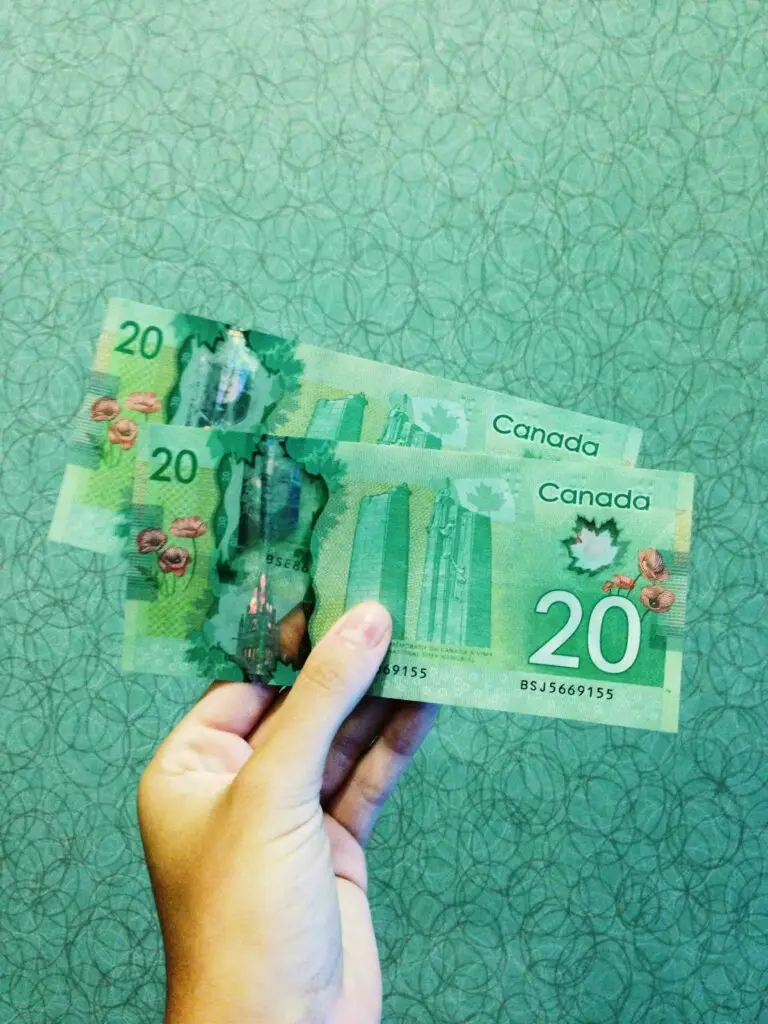 A hand holding two Canadian twenty-dollar bills against a green patterned background, perhaps counting the funds needed for an unexpected Emergency Locksmith Cost.