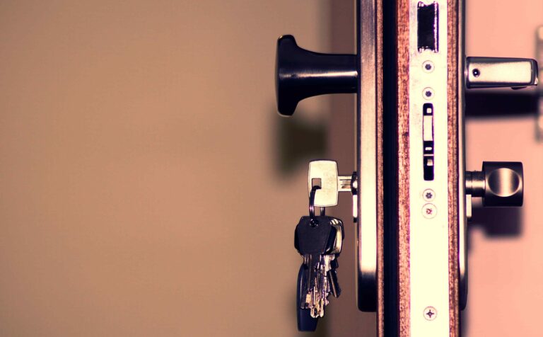 A close-up of a door’s locking mechanism with a set of keys inserted into the lock, shot from the side against a beige background, highlights the precision and security provided by a Reliable Locksmith Vancouver, specializing in residential locksmith services.